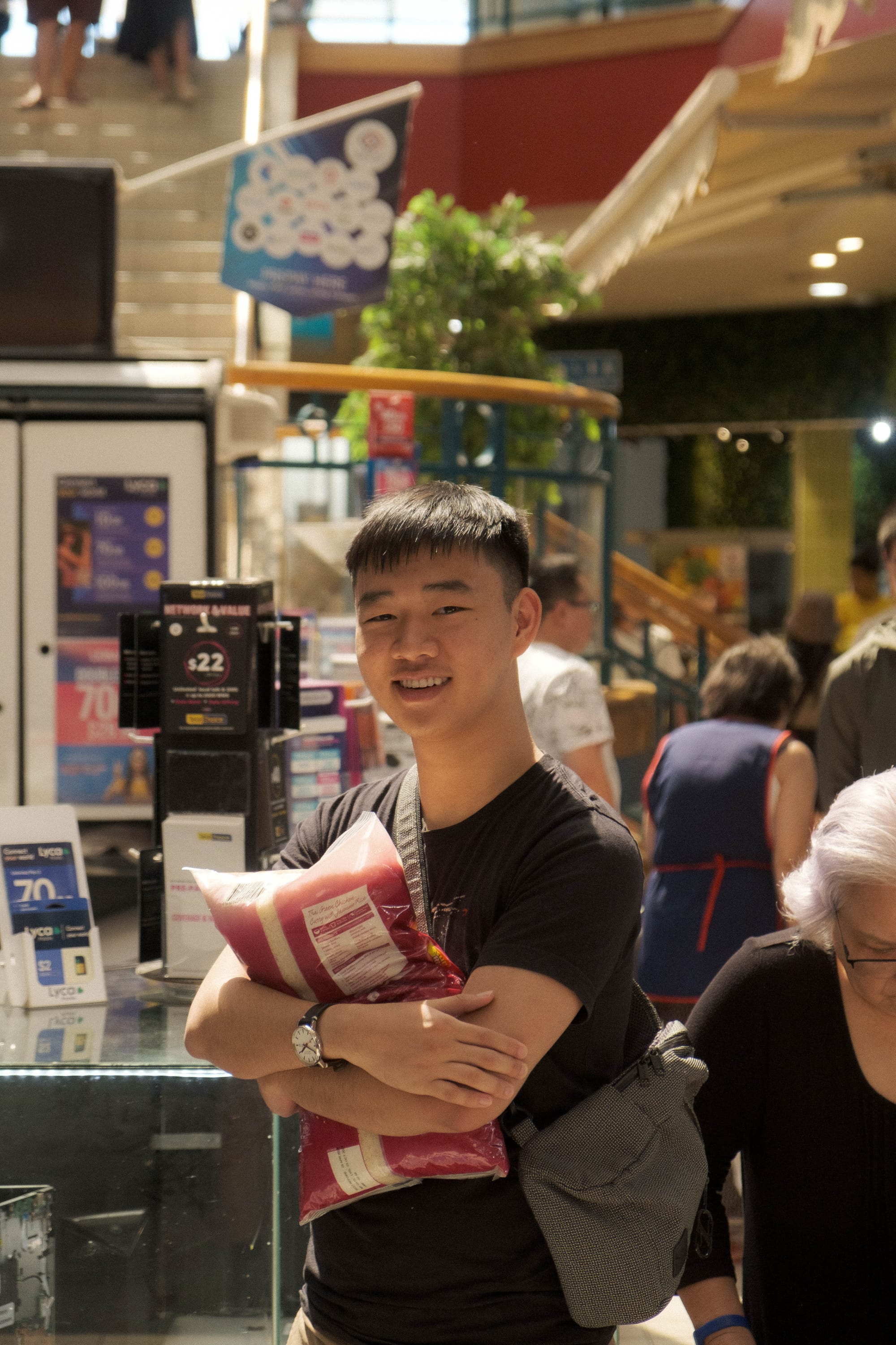 Nathan Wong standing in a Singapore mall, arms folded around a large bag of crisps