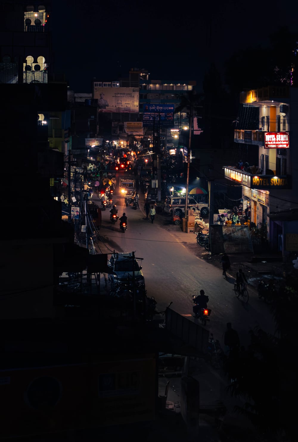Narrow street at night seen from above, hotel signs and motorbike headlights