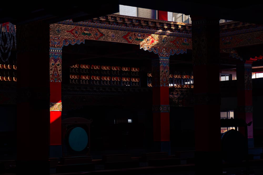 Unlit temple interior, painted beams and red columns catching a single shaft of light
